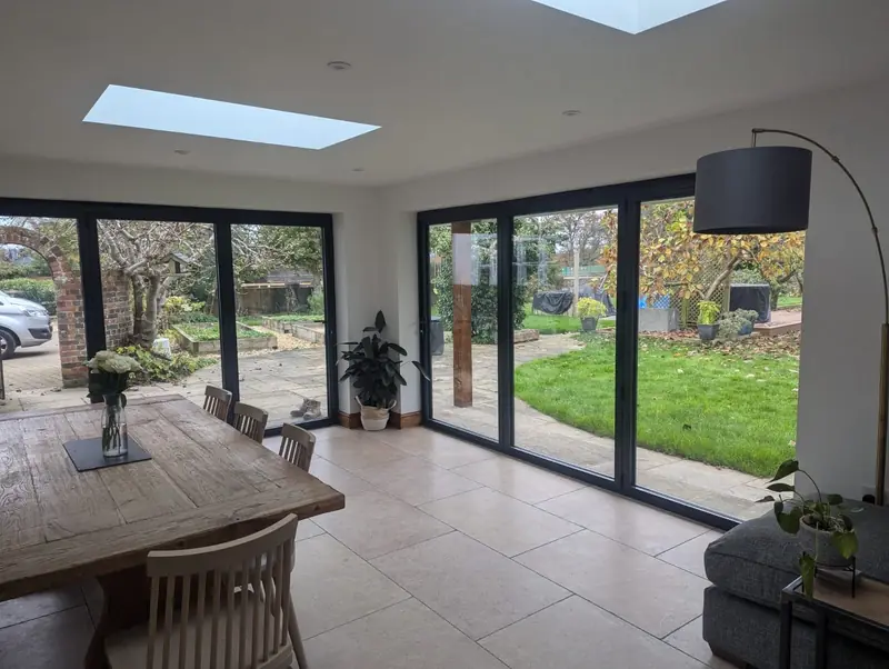 Inside a finished extension: a dining table under flat roof lights, with bi-fold doors along two walls
