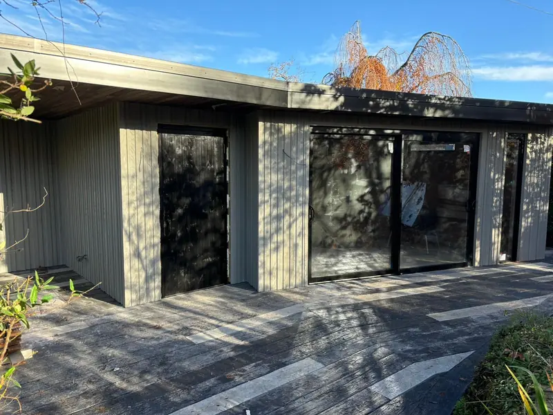A grey-clad garden room with sliding glass doors on a dark composite deck