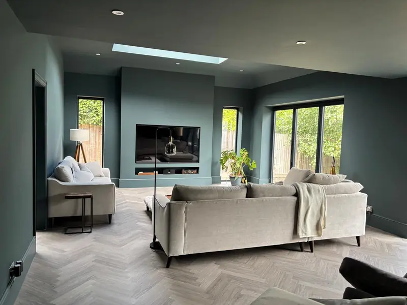 A finished living room with a roof light, herringbone floor and a built-in media wall