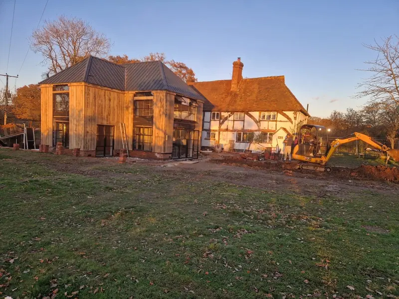 A two-storey timber-clad extension with a dark metal roof beside a timber-framed cottage at sunset